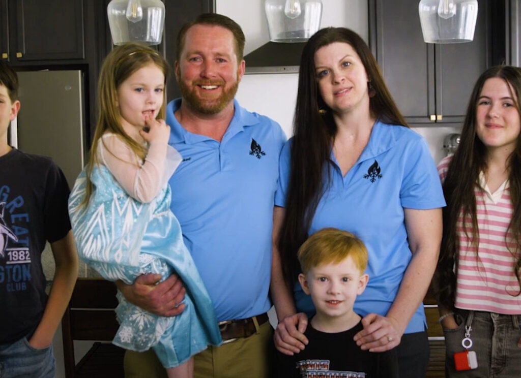 A smiling family of six standing together in a modern kitchen, with two adults wearing Proformance HVAC uniforms and four children gathered around them, representing the team behind the local Utah HVAC company.